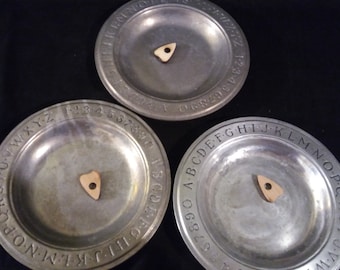 May include: Three silver plates with black lettering around the edges. Each plate has a small wooden planchette in the center. The plates are labeled with the alphabet, numbers 1-30, and the alphabet again.