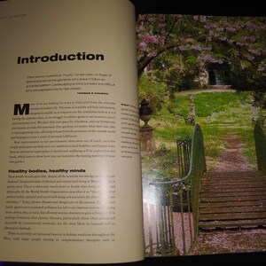 May include: An open book with a green, metal bridge in the background. The book is open to a page titled "Introduction" and discusses the importance of gardening for mental and physical well-being. The text reads, "There are no mysterious rules, no set rules, no finger of shame pointed at the gardener who doesn't follow an accepted pattern. Landscaping is not a complex and difficult art to be practiced only by high priests."