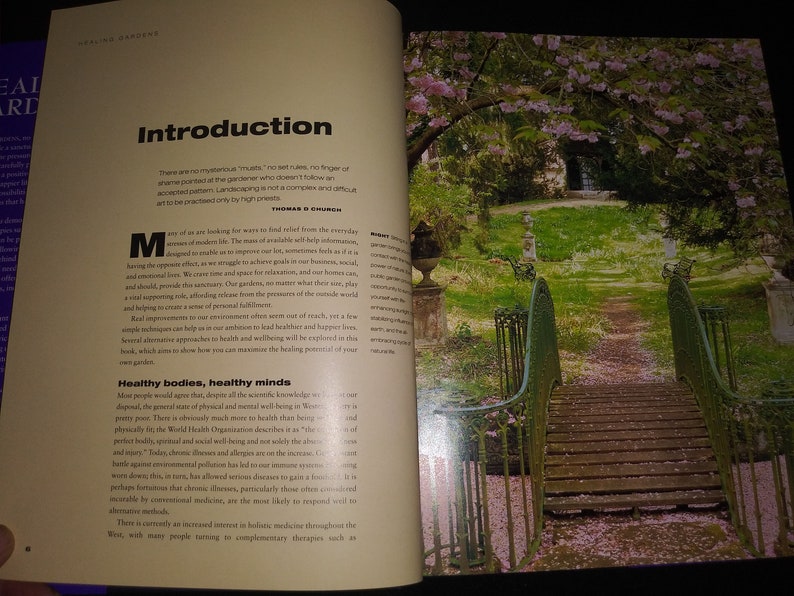 May include: An open book with a green, metal bridge in the background. The book is open to a page titled "Introduction" and discusses the importance of gardening for mental and physical well-being. The text reads, "There are no mysterious rules, no set rules, no finger of shame pointed at the gardener who doesn't follow an accepted pattern. Landscaping is not a complex and difficult art to be practiced only by high priests."