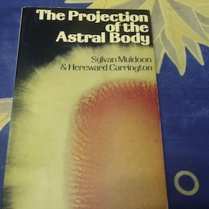 Puede incluir: Un libro antiguo titulado "The Projection of the Astral Body" de Sylvan Muldoon y Hereward Carrington. El libro tiene una cubierta azul oscuro con texto blanco y un diseño abstracto amarillo y rojo. El libro está sobre un fondo azul con patrones de estrellas y luna.