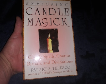 May include: A book titled "Exploring Candle Magick" by Patricia Telesco, author of "A Witch's Beverages and Brews". The cover features a lit candle in a window frame against a pink background.