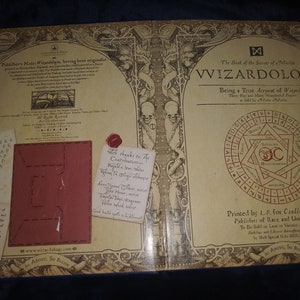 May include: An open book, "Wizardology", with intricate illustrations and text. The cover displays ornate designs, skulls, and a central circular emblem. Includes a red leather insert and handwritten notes.