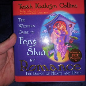 May include: Purple book cover with gold lettering that reads "The Western Guide to Feng Shui for Romance: The Dance of Heart and Home." The cover features a couple dancing in front of a house with a purple roof and a red door. The book includes a free meditation CD.