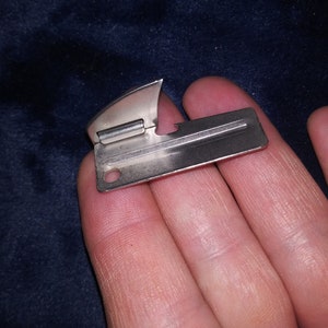 May include: A silver can opener with a small handle and a sharp blade. The opener is designed to open cans of food.