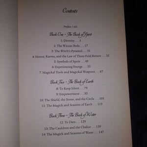 May include: A book titled "The Book of Spirit" with a table of contents listing chapters on divinity, the Wiccan Rede, the Witch's Pyramid, honor, karma, and the law of three-fold return, symbols of spirit, experiencing energy, and magickal tools and weapons.