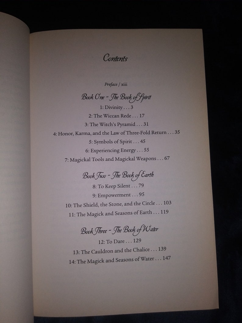 May include: A book titled "The Book of Spirit" with a table of contents listing chapters on divinity, the Wiccan Rede, the Witch's Pyramid, honor, karma, and the law of three-fold return, symbols of spirit, experiencing energy, and magickal tools and weapons.