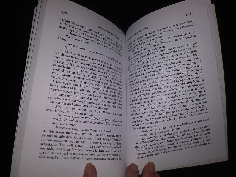 May include: A close-up of an open book with a white background. The book is open to a page with the title "Guide to Past Life Regression" and the text "What caused you to become aware that you were dead?" The page also includes text about the experience of death and the process of regression.