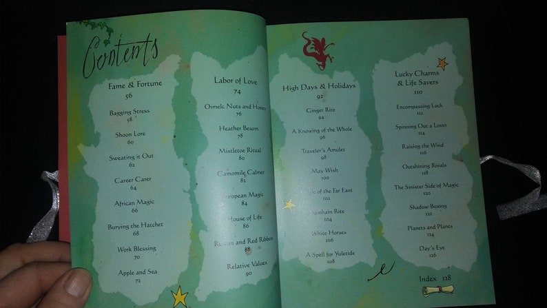 May include: An open book with a green and blue watercolor background. The book's contents page lists various topics, including "Fame & Fortune", "Labor of Love", "High Days & Holidays", and "Lucky Charms & Life Savers".