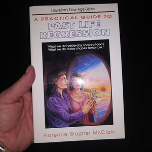 May include: A white book with a blue and purple illustration of two women looking at each other in a mirror. The book title is "A Practical Guide to Past Life Regression" and the author is Florence Wagner McClain. The book is part of Llewellyn's New Age Series.