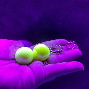 May include: Two bright yellow glass marbles and two silver rings on a hand against a purple background.