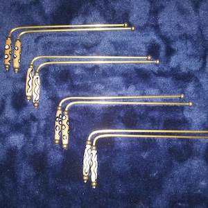 May include: Five gold-colored metal curtain tiebacks with black and white patterned wooden handles. The handles have different patterns, including polka dots, wavy lines, and abstract designs.