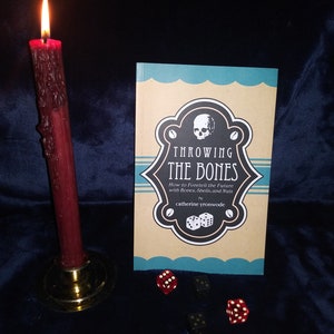 May include: A book titled "Throwing the Bones: How to Foretell the Future with Bones, Shells, and Nuts" by catherine yronwode. The book cover features a skull and dice in a black and white illustration with a teal and brown background.