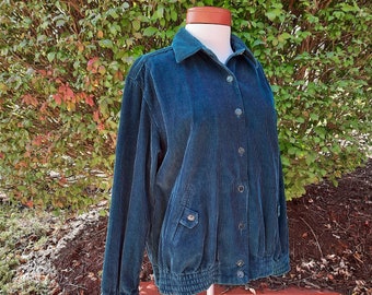 May include: Teal corduroy jacket with a button-up front, two front pockets, and a ribbed hem and cuffs. The jacket is displayed on a mannequin with a brown neck. The background features green foliage.