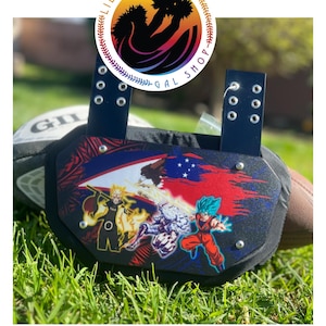 May include: A black football back plate featuring a graphic print of anime characters, including a yellow-haired figure and a blue-haired figure, set against a red and blue background with a Samoan flag design and two vertical attachment straps.