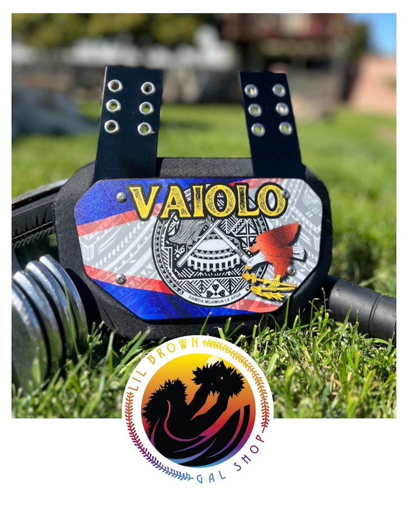 May include: A black sports chest protector featuring a central plate with the name VAIOLO in yellow text, a graphic of a red eagle, and a circular emblem with Samoan patterns. The plate is attached to black straps with silver metal eyelets.