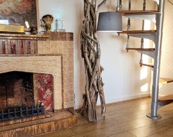 May include: A unique floor lamp crafted from driftwood, featuring a gray lampshade. The lamp stands next to a spiral staircase and a fireplace with a decorative mantel. The room has hardwood flooring.