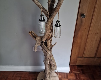 May include: A rustic floor lamp made from driftwood with two hanging glass jars with lights inside. The lamp is on a wooden base and has a natural, organic look.