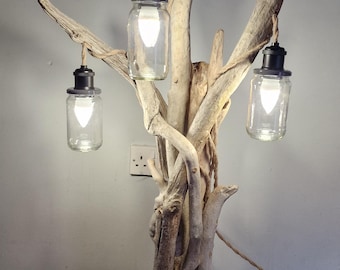 May include: A unique driftwood lamp with three clear glass jar shades. The lamp is mounted on a wooden base and features a natural, rustic design. The light fixtures are suspended from the driftwood branches, creating a warm, inviting glow.