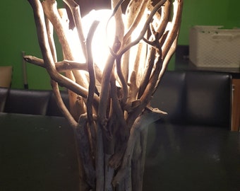 May include: A table lamp made from driftwood branches with a white light bulb. The lamp is lit and casting a warm glow.