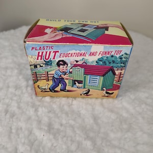 May include: A vintage toy box with the words "PLASTIC HUT EDUCATIONAL AND FUNNY TOY" printed on the front. The box features illustrations of a child, a green hut, and farm animals. The top of the box reads "BUILD YOUR OWN HUT."