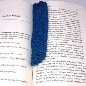 Może przedstawiać: Zbliżenie na niebieską zakładkę na drutach z gradientem od ciemnoniebieskiego do jasnoniebieskiego. Zakładka znajduje się w otwartej książce z tekstem o książkach i bibliotekach.