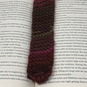 Może przedstawiać: Zbliżenie na brązową, zieloną i różową zakładkę na książkę wykonaną na szydełku, z widoczną stroną książki w tle. Na stronie książki widnieje tekst "Brave Love" i "Beauty Matters".