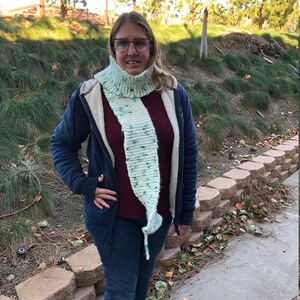 Może przedstawiać: Kobieta w niebieskiej kurtce z kapturem, bordowej koszuli, niebieskich dżinsach i długim, białym i zielonym dzianym szaliku z wzorami w kropki.