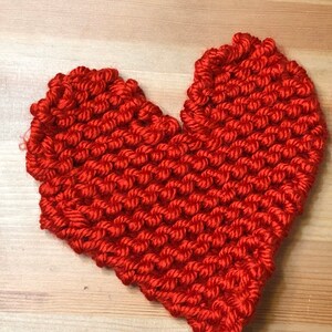 Może przedstawiać: Ręcznie robione czerwone serduszko z włóczki, na drewnianej powierzchni.