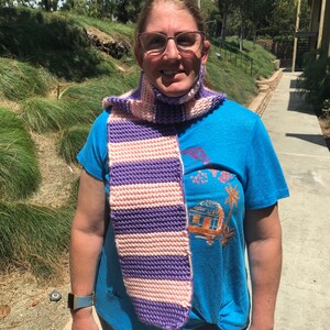 Może przedstawiać: Kobieta w niebieskiej koszuli z różowo-fioletowym paskowanym szalikiem. Szalik jest dziergany na drutach i ma długi, prostokątny kształt.