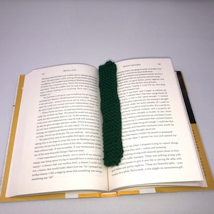 Może przedstawiać: Zielony, dzianinowy zakładka z fakturowanym wzorem umieszczona między stronami otwartej książki. Książka nosi tytuł "Brave Love" i "Reality Matters".