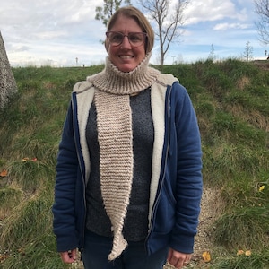 Może przedstawiać: Kobieta w niebieskiej kurtce z brązowo-białym dzianym szalikiem. Szalik jest długi i ma spiczasty koniec.