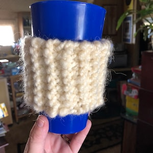 Może przedstawiać: Biały dzianinowy ocieplacz do kubka z niebieskim plastikowym kubkiem w środku.