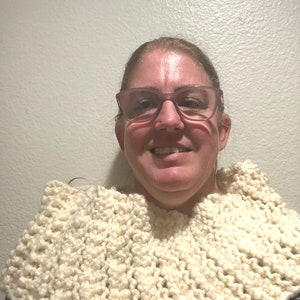 Może przedstawiać: Kobieta w białym dzianym kominie. Komin wykonany jest z grubego włóczki i ma fakturowany wzór ściegu.