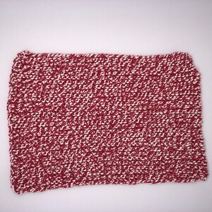 Może przedstawiać: Prostokątna, ręcznie robiona ściereczka lub mały koc. Przedmiot jest mieszanką bordowej i białej przędzy, tworzącą teksturowaną, wzorzystą powierzchnię. Krawędzie są lekko nierówne, co wskazuje na ręcznie robiony przedmiot.