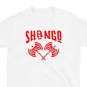 May include: White t-shirt with a red graphic design of the word "SHANGO" and two stylized axes.