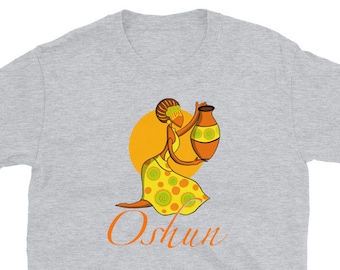 Könnte beinhalten: Graues T-Shirt mit einem Motiv einer Frau in einem gelben und grünen Kleid, die einen braunen Topf hält. Der Text "Oshun" ist in Orange unter dem Motiv gedruckt.