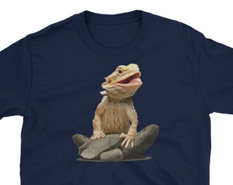 Op de afbeelding: Een marineblauw t-shirt met een afbeelding van een baardagame die op een rots zit. De draak heeft zijn bek open en kijkt omhoog.