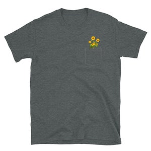 May include: A dark heather grey t-shirt with a pocket featuring a small bouquet of yellow sunflowers.