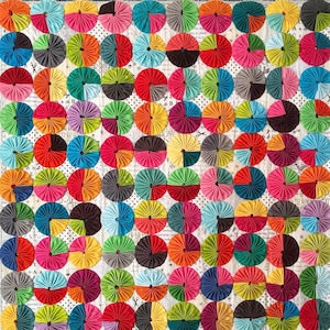 Może przedstawiać: Kolorowa kołdra z powtarzającym się wzorem żywych, okrągłych kół. Koła ułożone są w siatkę i wykonane są z różnych kolorów, w tym czerwonego, niebieskiego, zielonego, żółtego i różowego. Tło jest jasne z nadrukowanym tekstem.