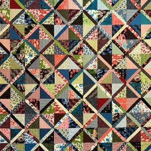 Pode incluir: Um edredom de retalhos com um design geométrico. O edredom apresenta uma variedade de tecidos em tons de azul, verde, rosa e castanho. O padrão é composto por triângulos e quadrados, criando um têxtil visualmente interessante e colorido.