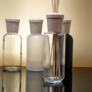 May include: Five glass bottles with wooden stoppers and a variety of finishes, including clear, frosted, and black. Some bottles have wooden sticks inserted into them.