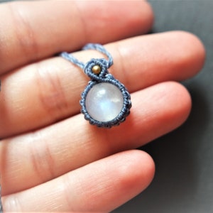 Puede incluir: Un collar de cordón azul con un colgante de piedra lunar. El colgante está envuelto en cordón azul y tiene un pequeño acento de cuentas doradas.