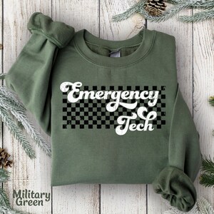 May include: A green sweatshirt with a white checkered background and the text "Emergency Tech" in a retro font.