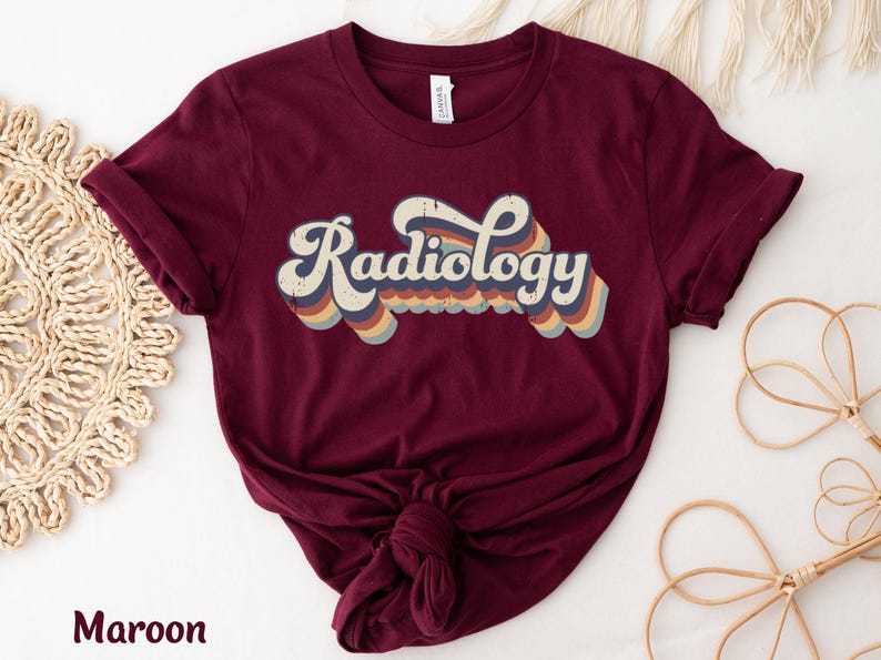 May include: Maroon t-shirt with the word "Radiology" in a retro font. The text is in white with a layered design of blue, orange, and yellow stripes. The shirt is knotted at the bottom.