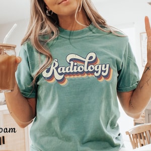 May include: Seafoam green t-shirt with a retro-style graphic that says "Radiology" in rainbow colors.