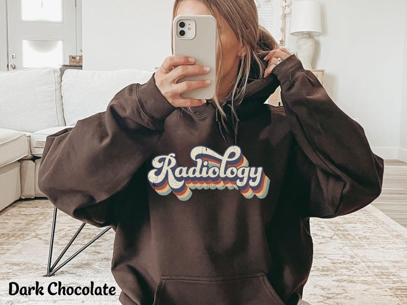 May include: Dark chocolate-colored hoodie with the word "Radiology" in a retro font across the chest. The text has a layered design with red, orange, yellow, and blue accents. The hoodie has a front pocket and a hood.