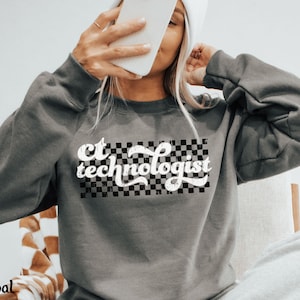 May include: Charcoal gray sweatshirt with the text "CT technologist" in a white, retro font over a black and white checkered design. The sweatshirt has long sleeves and a crew neck.