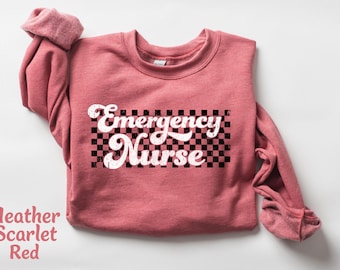 May include: Heather scarlet red sweatshirt with a white graphic that says "Emergency Nurse" in a retro font with a black and white checkered background.