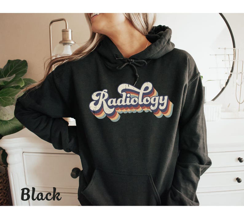 May include: Black hoodie with the word "Radiology" in a retro font, featuring a white outline and rainbow-colored accents. The hoodie has a drawstring hood and a front pocket. The word "Black" is printed at the bottom left.