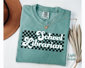 Può includere: Maglietta verde chiaro con un motivo a scacchi bianchi e il testo "School Librarian" in un font retrò.